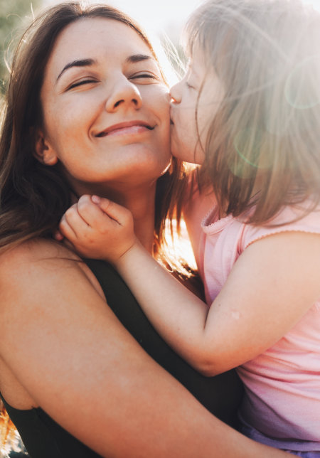 Young girl kissing smiling woman on the cheek outdoors.